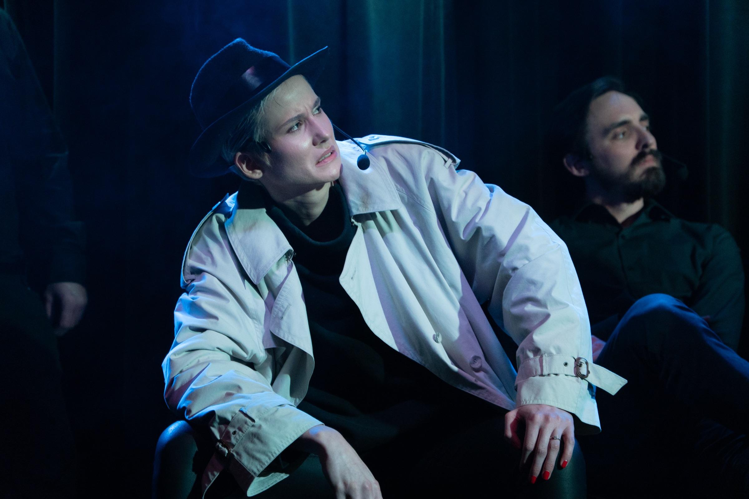 Improv scene with a performer in a trench coat and fedora