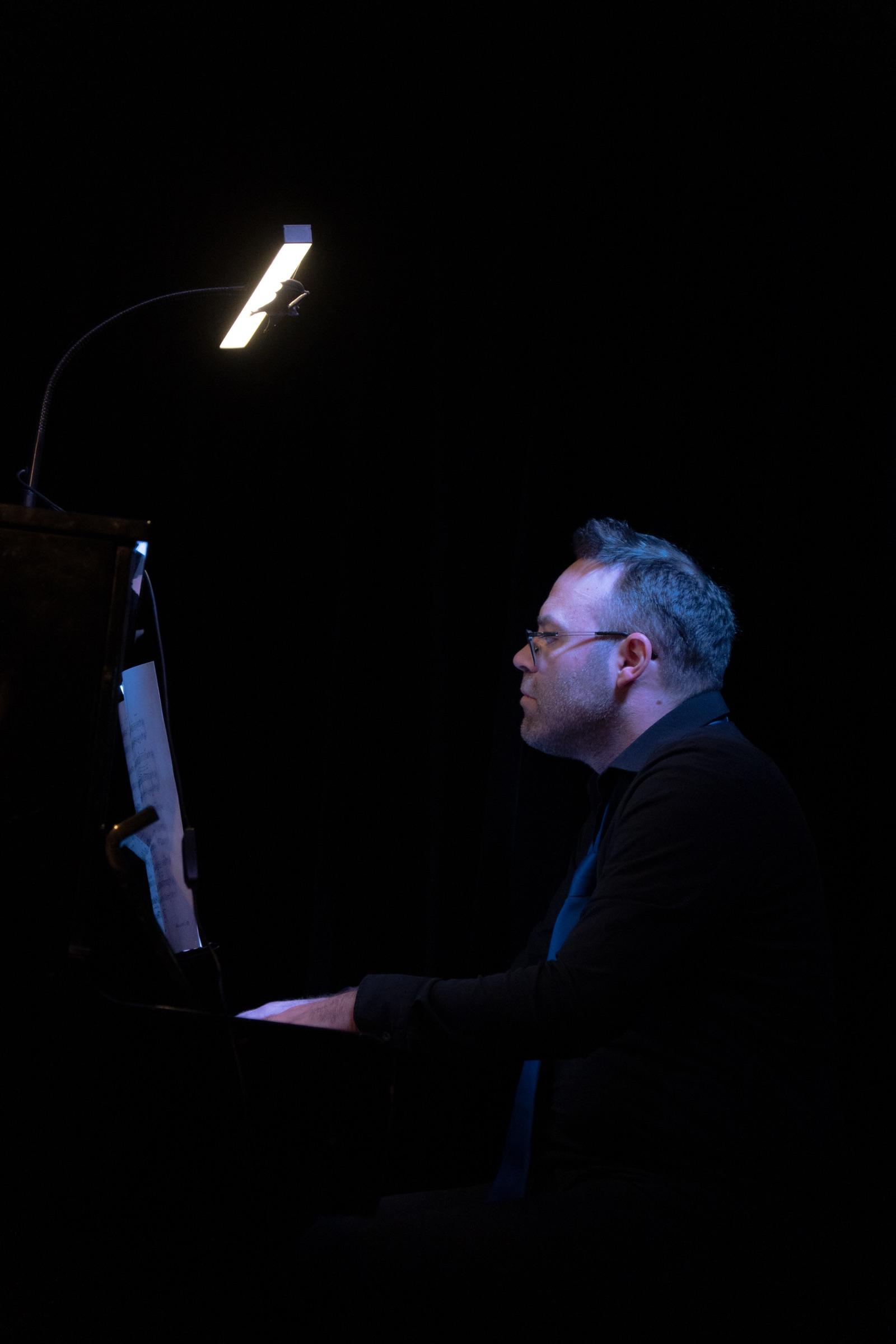 Accompanist at the piano lit by a single lamp on a dark stage