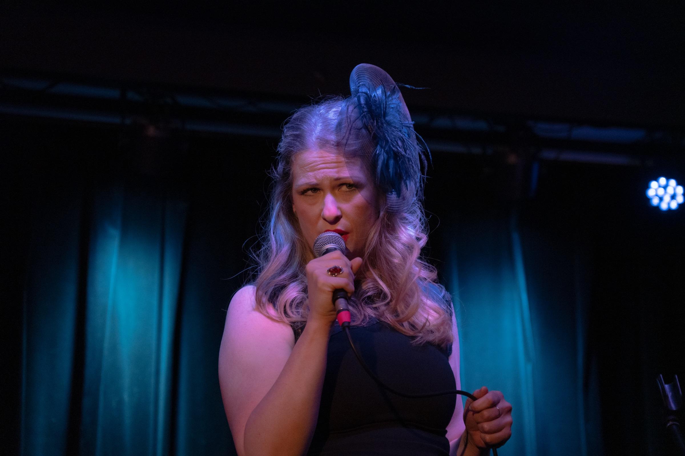 Performer in a feathered headpiece singing on a dim stage