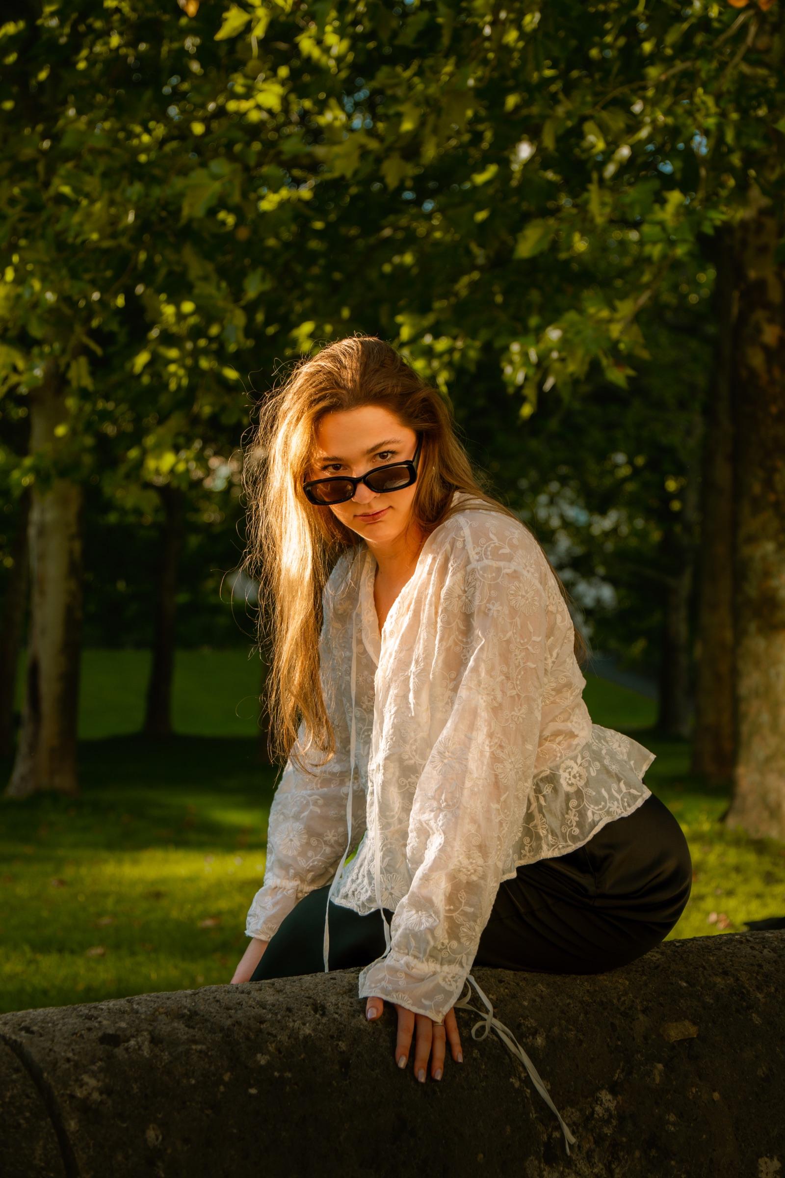 Portrait of a woman crouching on a stone wall wearing sunglasses