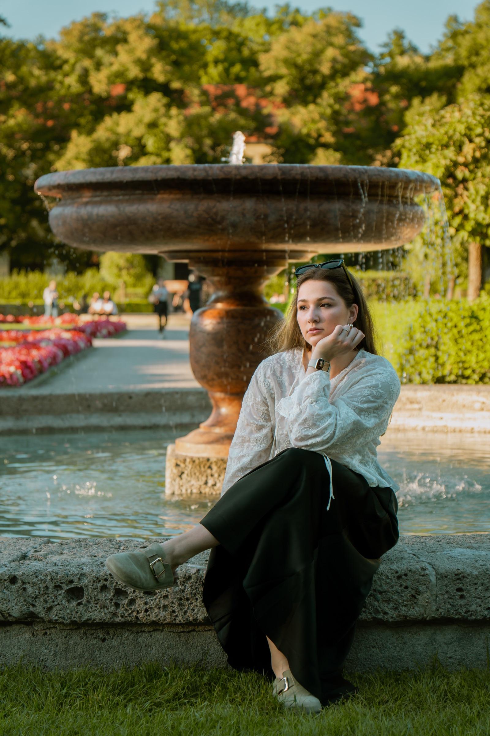 Portrait of a woman seated by a fountain in a formal garden
