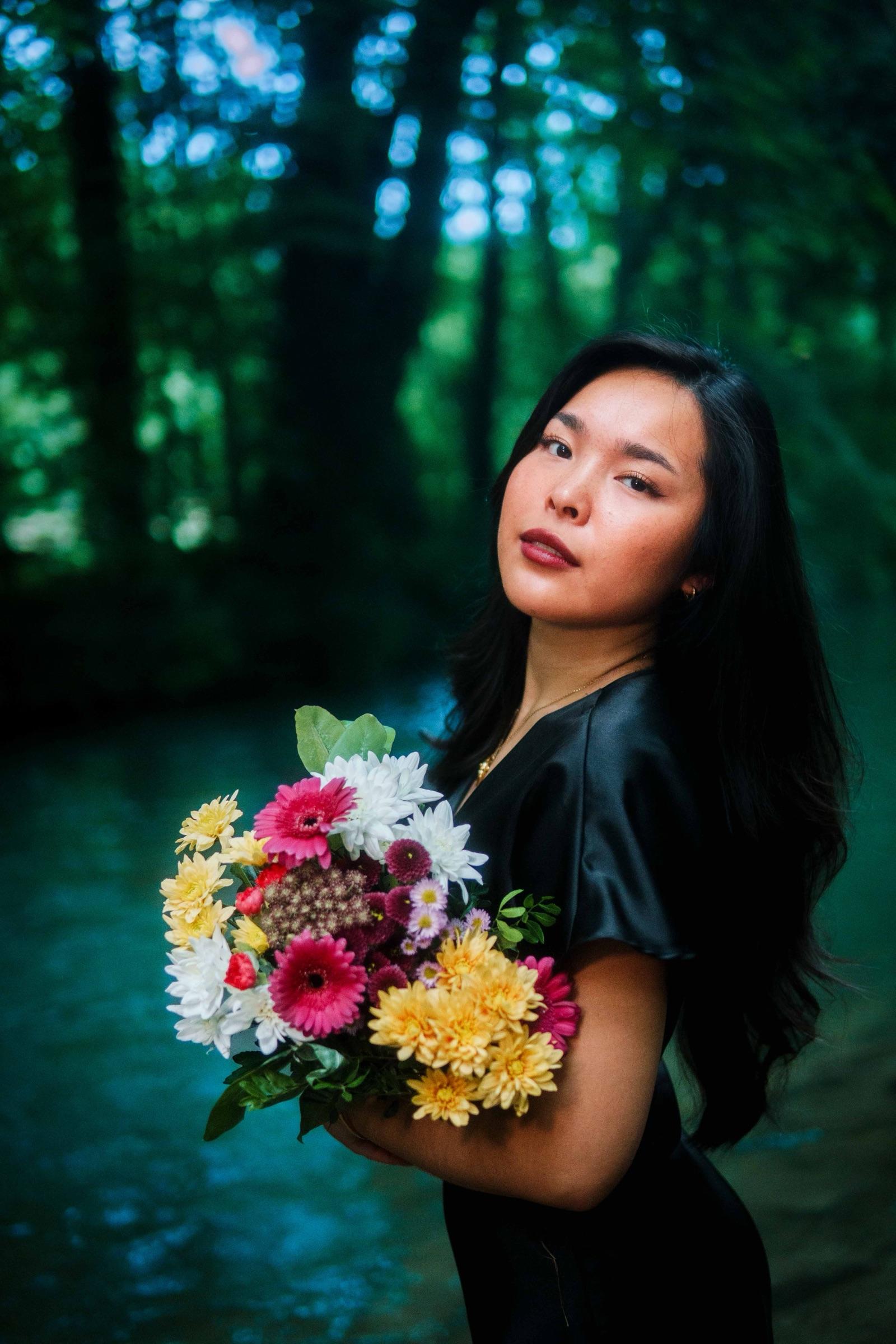 Woman holding a wildflower bouquet beside a forest river, looking back at the camera