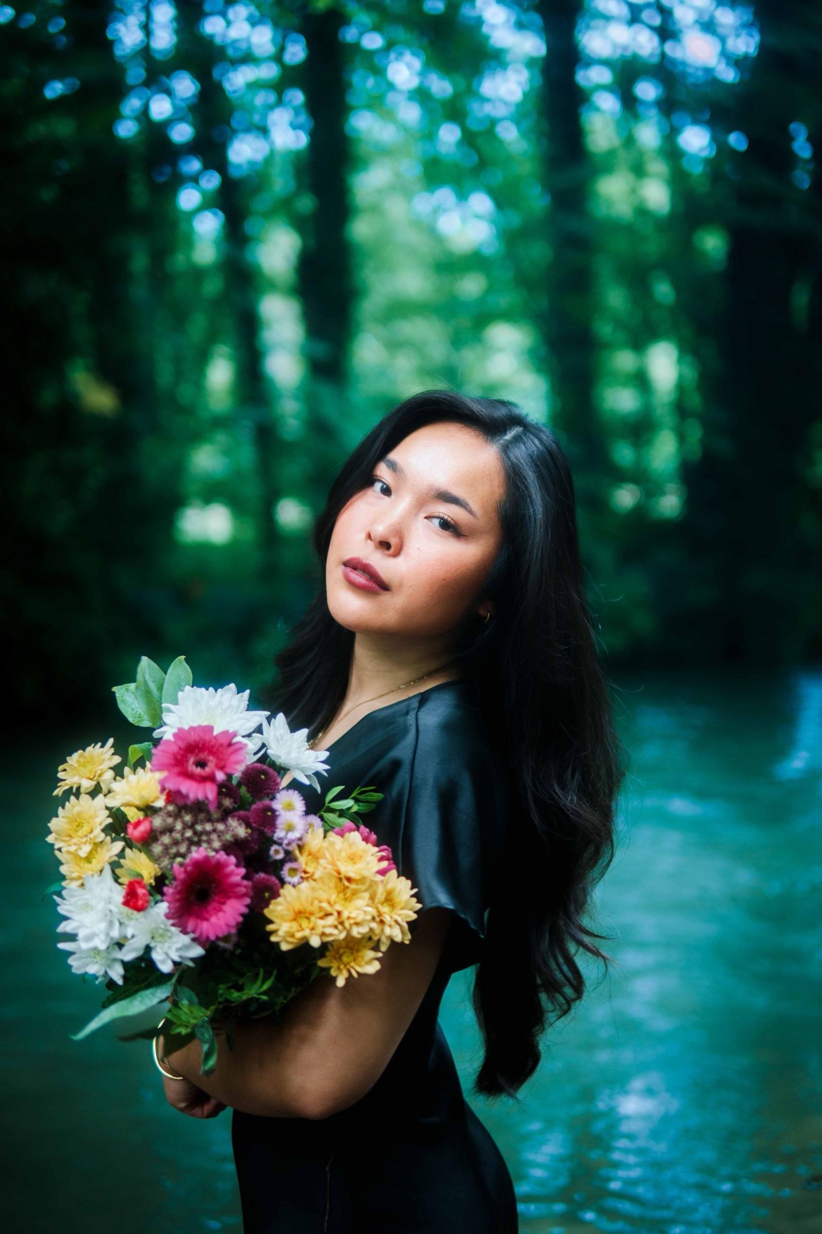 Woman in black turned toward the river, holding a bouquet
