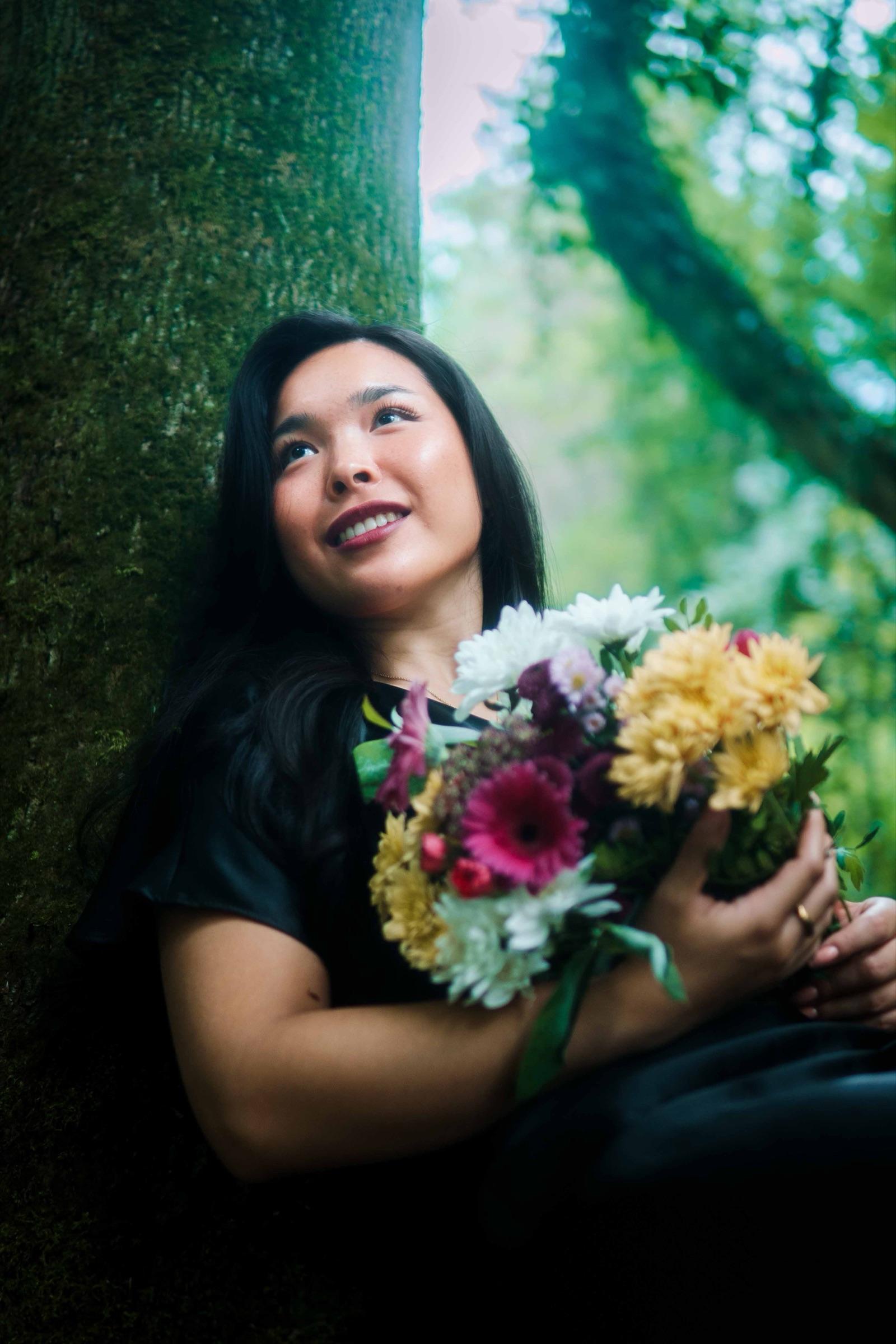 Woman laughing as she holds a bouquet against a mossy tree