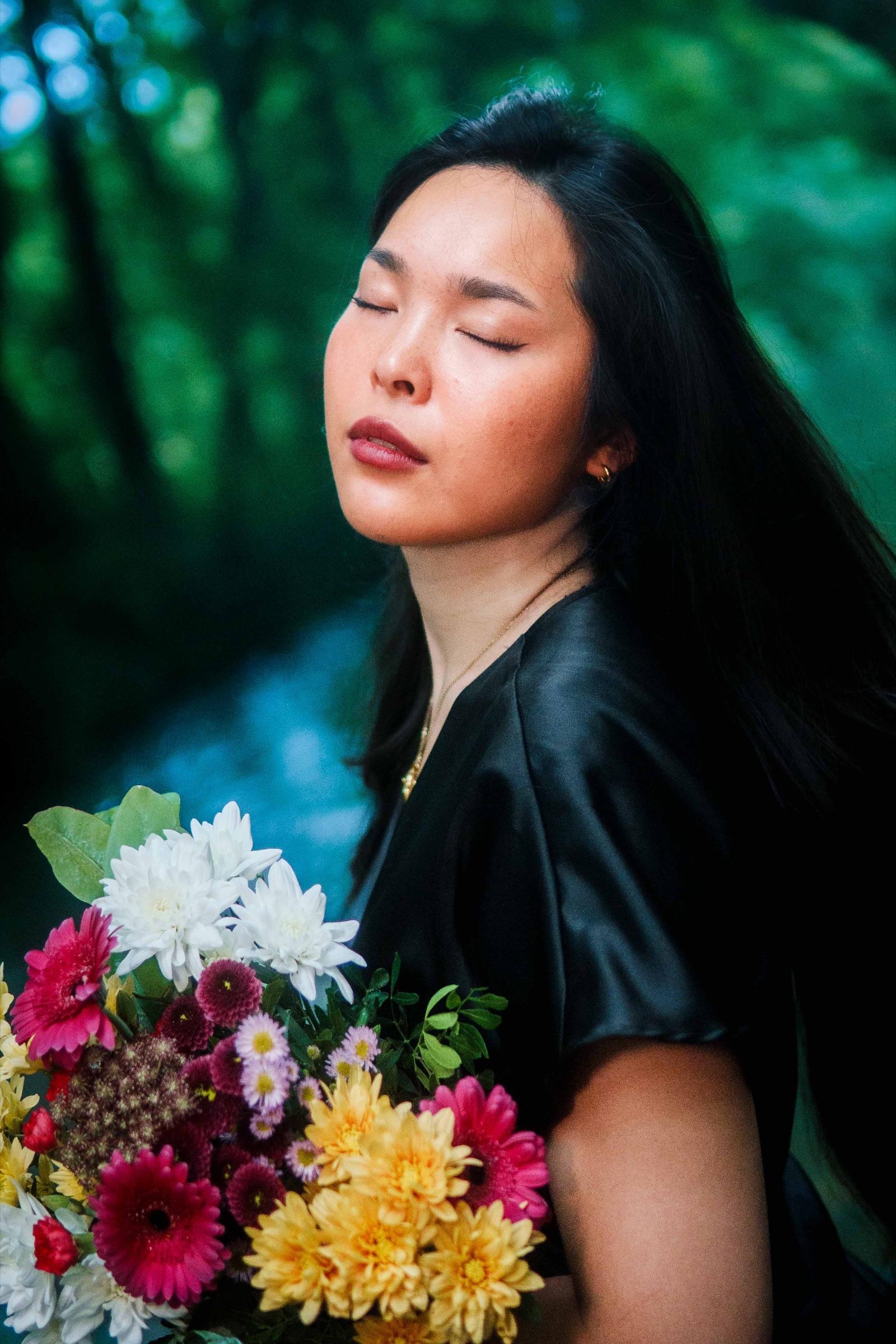 Woman with her eyes closed, holding a bouquet in the forest
