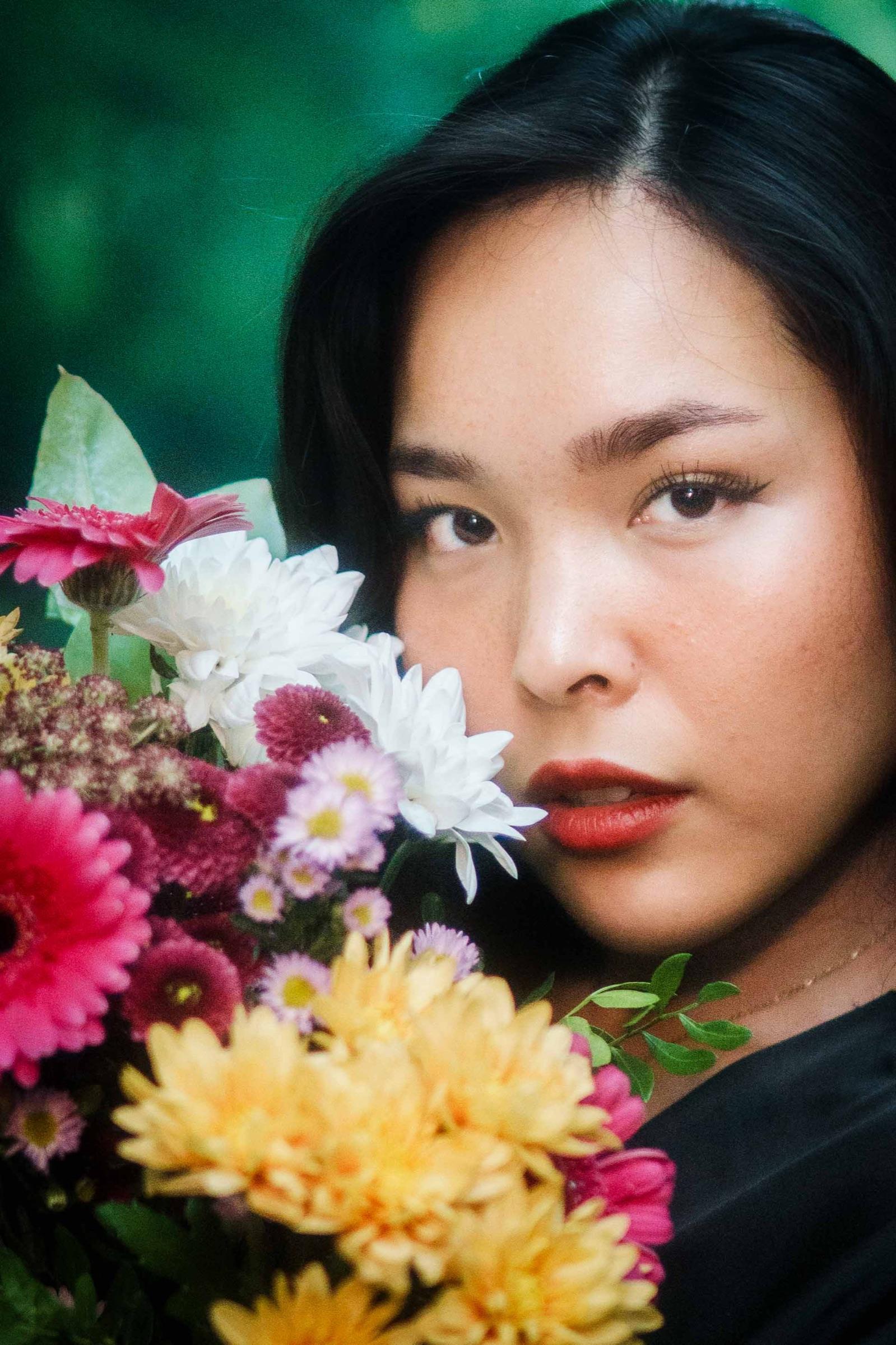 Close portrait of a woman beside a bright bouquet, looking straight at the camera
