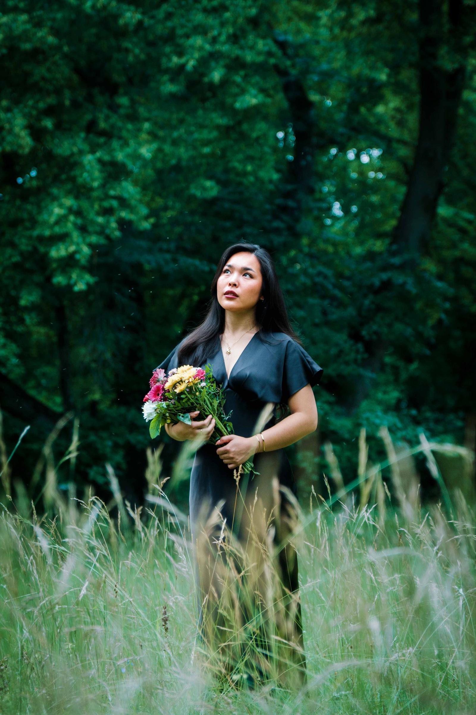 Woman in a black dress standing in tall summer grass, looking up