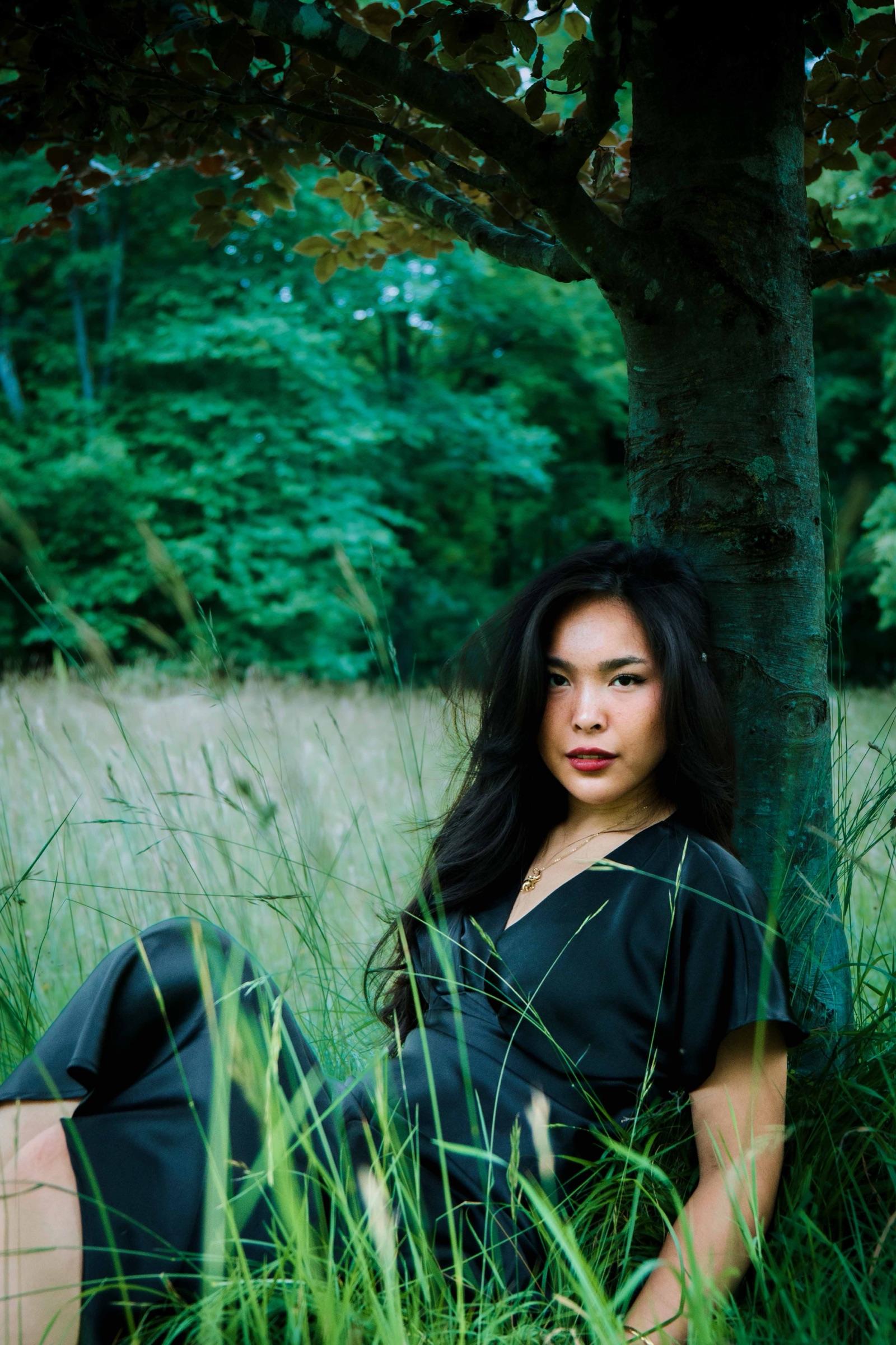 Woman seated beneath a tree in a meadow, looking at the camera