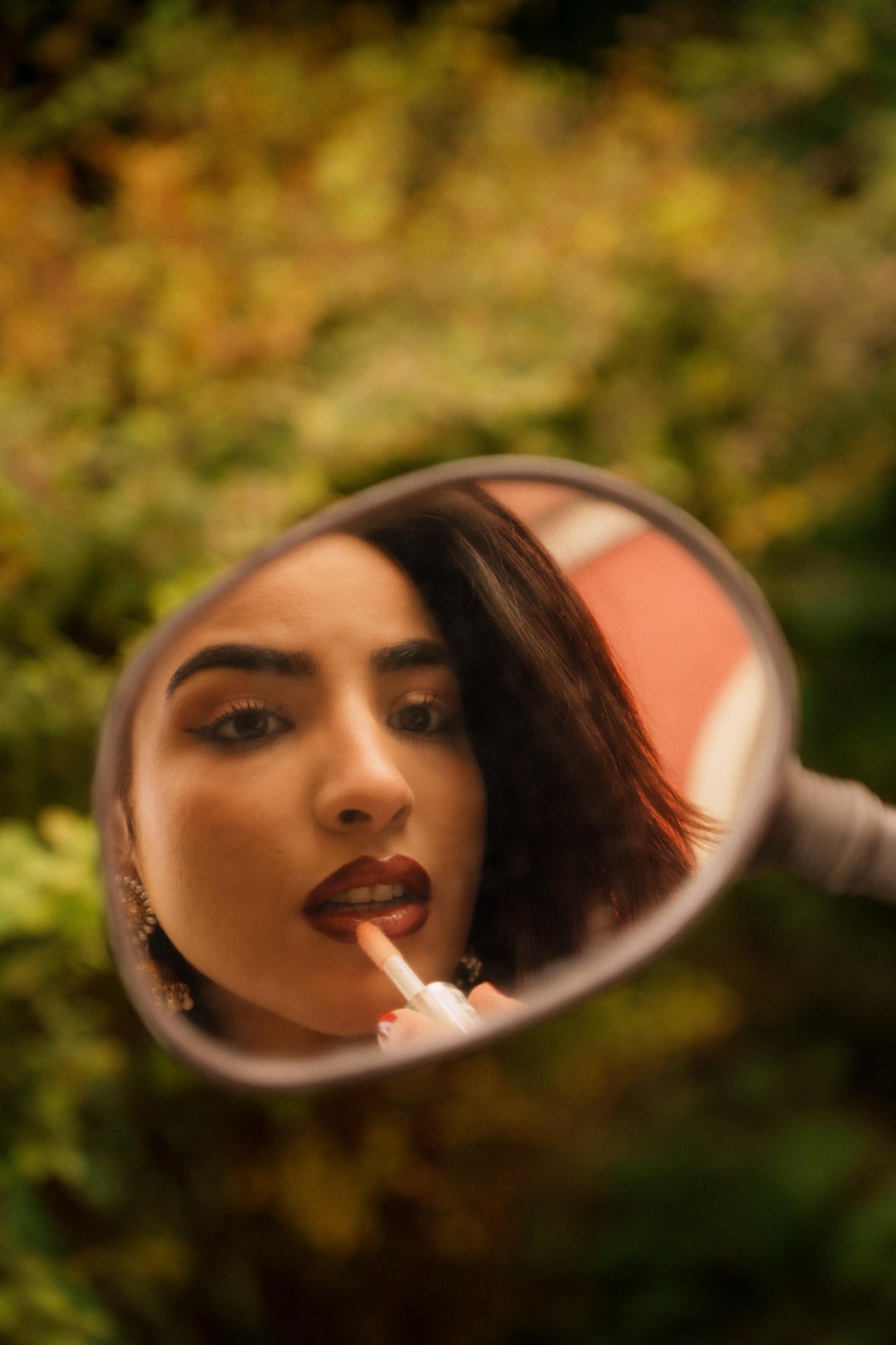 Portrait reflected in a hand mirror, applying lipstick