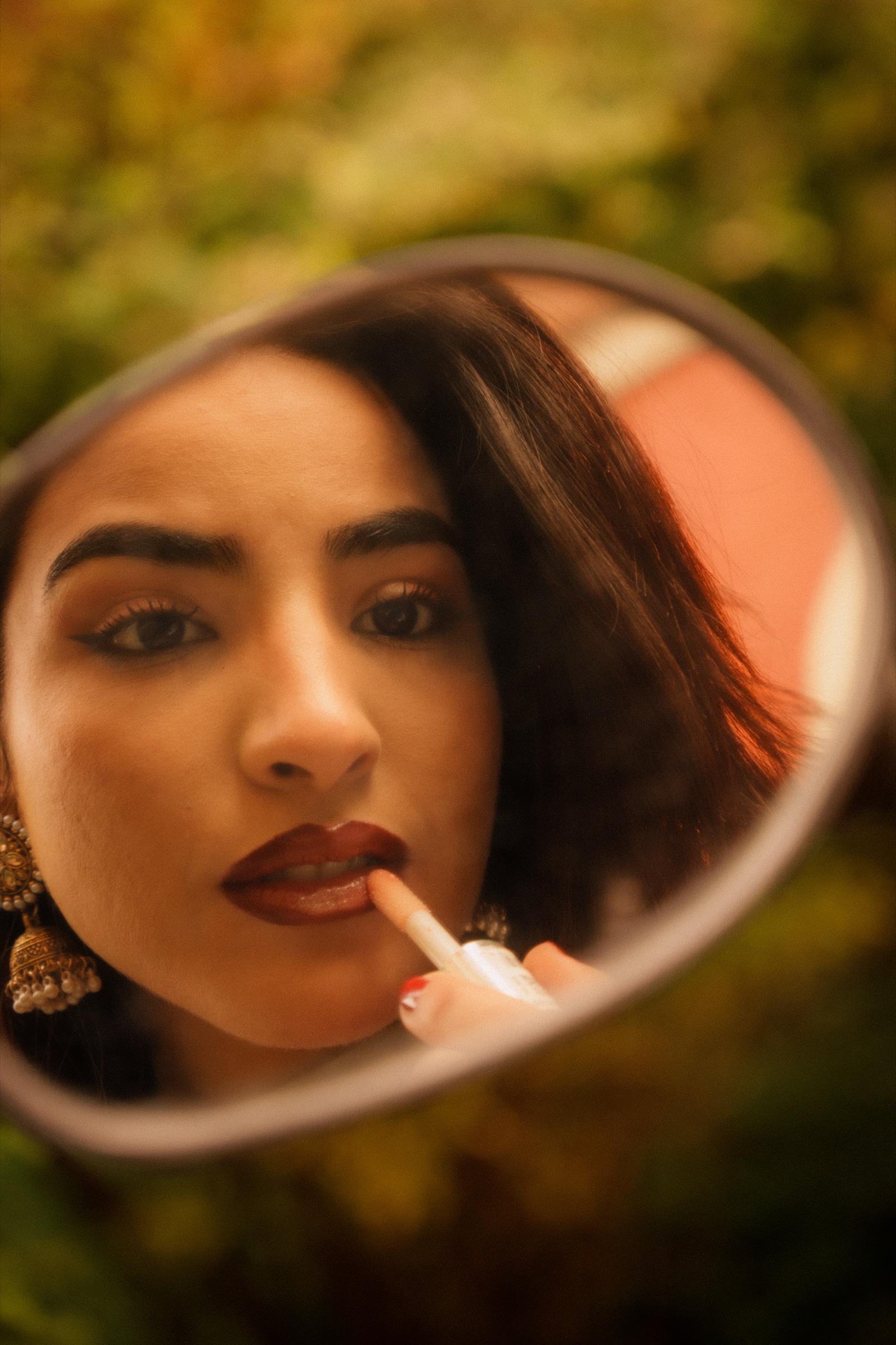 Woman applying lipstick, reflected in a round hand mirror