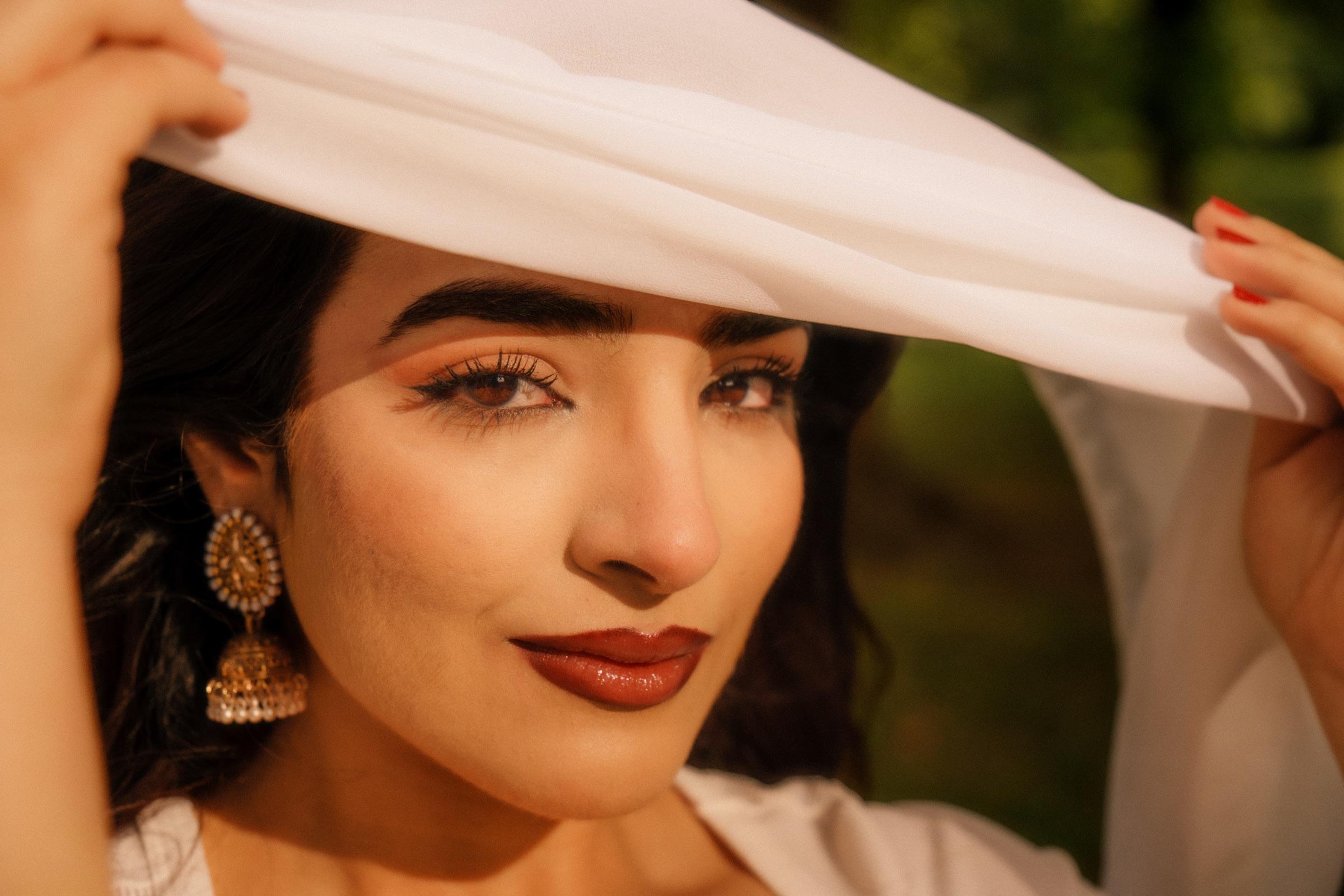 Editorial portrait of a woman lifting a white scarf like a veil