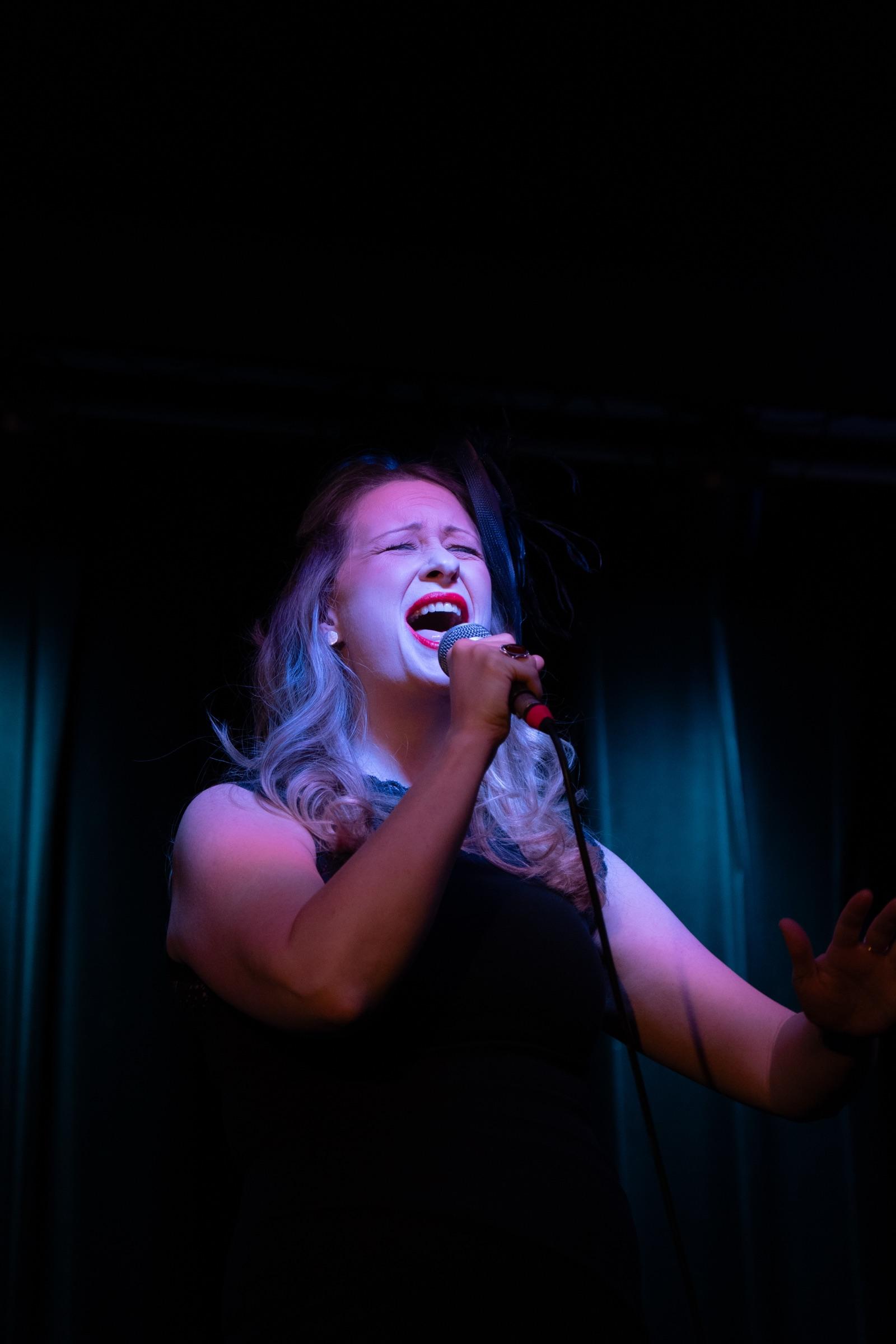 Singer belting into a microphone under a moody spotlight